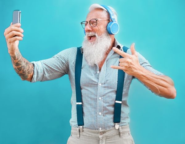 Senior hipster man using smartphone app for creating playlist with rock music - Trendy tattoo guy having fun with mobile phone technology - Tech and joyful elderly lifestyle concept - Focus on face